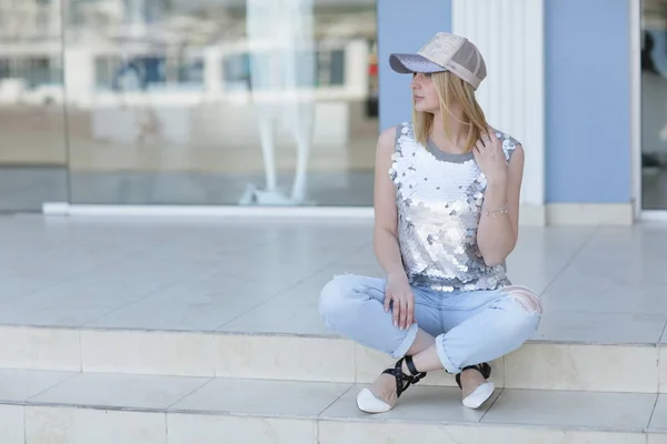 A woman in casual clothes sits on the steps near the shop Windows — ストック写真