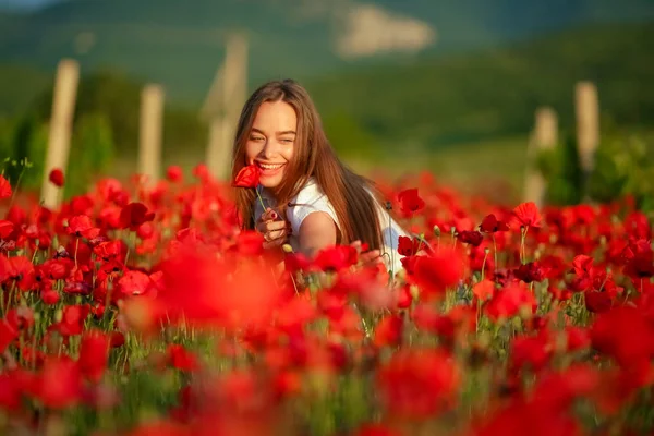 The woman crouched in a field of poppies so that only her head with brown hair was visible — 스톡 사진