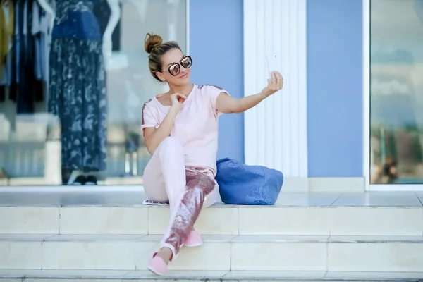Eine Frau mit Brille sitzt auf der Treppe und macht ein Selfie mit ihrem Handy — Stockfoto