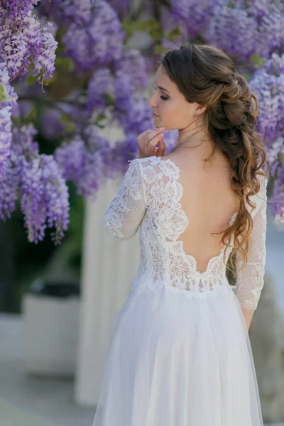 En brud i bröllopsklänning står med ryggen mot kameran under ett träd — Stockfoto