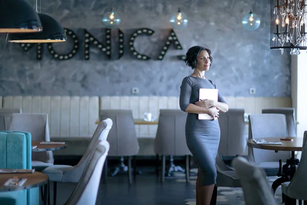 An adult woman stands facing the camera and holds a folded laptop in front of her