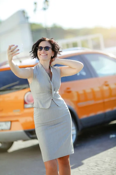 Una mujer adulta en un traje de negocios se toma una selfie en un aparcamiento —  Fotos de Stock