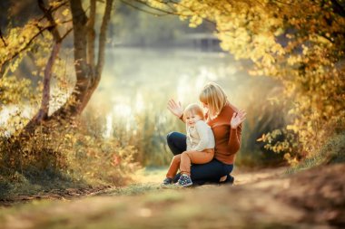 Mother and daughter squatting and playing among the trees on the background of a forest lake