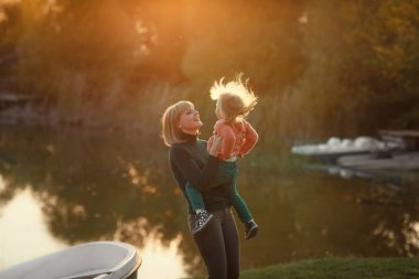 Anne, sonbaharda kızıyla gölün kenarında gün batımı ışınlarının arka planında eğleniyor.