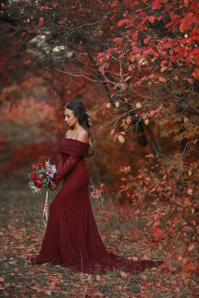 Uma mulher uma noiva jovem em um vestido de noiva vermelho com ombros delicados nus segurando um buquê de casamento — Fotografia de Stock