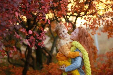 Genç bir kadın, yetişkin oğluyla sonbaharda ormanda yürür..
