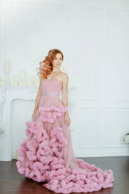 Pembe bir gelinlik içinde beyaz bir odanın arka planında büyüyen bir kadın model.