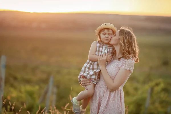 En mor med ett barn i famnen står högt på ett fält vid solnedgången med ett barn i famnen. — Stockfoto