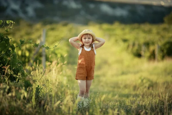 Egy vidám lány kalapban sétál egy fiatal mezőn, alacsony zöld fűvel. — Stock Fotó