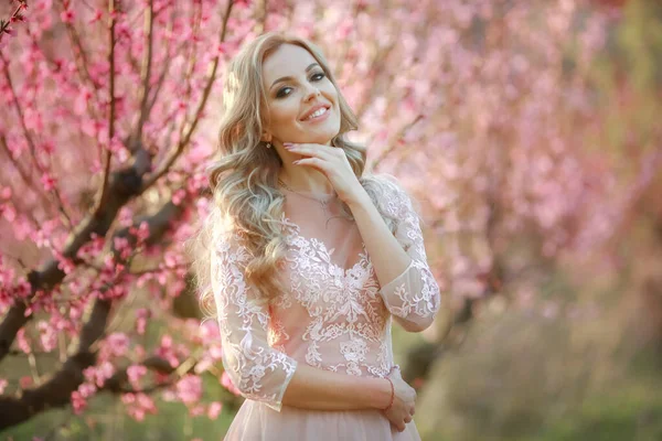 Braut am Hochzeitstag allein im langen rosa Kleid im blühenden Garten — Stockfoto