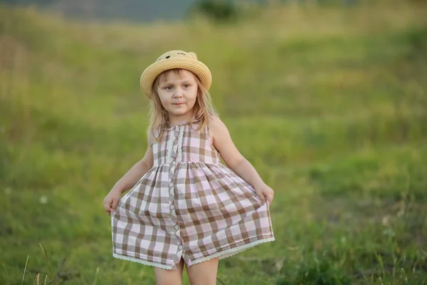 A cheerful girl in a hat walks on a young field with low green grass — Stock Photo, Image