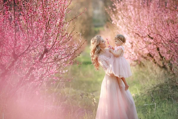 Dziecko 3-4 lata w różowej sukience w wiosennym ogrodzie kwitnącym w ramionach matki — Zdjęcie stockowe
