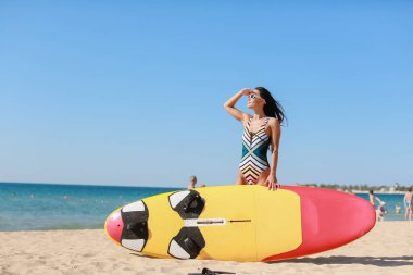 Güzel bir kadın kumlu bir sahilde, arka planda güneş gözlükleriyle...