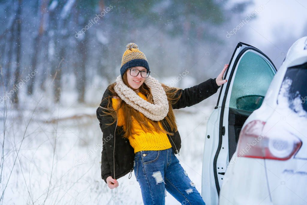 Woman in winter in a snowy field near a white car