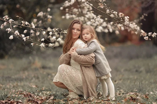 Baby hugs mom amid white blossoming trees — Stock Photo, Image