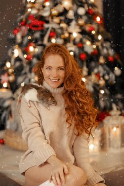 Elinde fare olan bir kadın Noel ağacının yanında oturuyor..