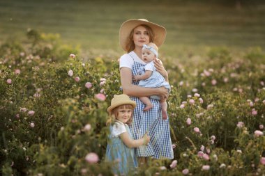 Çocuklu güzel bir anne elinde çiçeklerle bir tarla tarlasında duruyor.