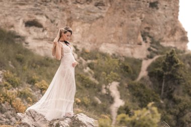 Hamilelik boyunca romantik bir yürüyüş yapan gelin yazın kayalıklarda yürüyor.