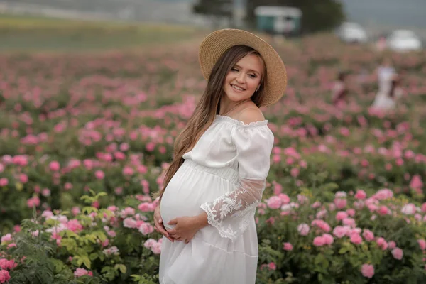 Pregnant woman in straw hat on her head stands in a flower field — Stock fotografie