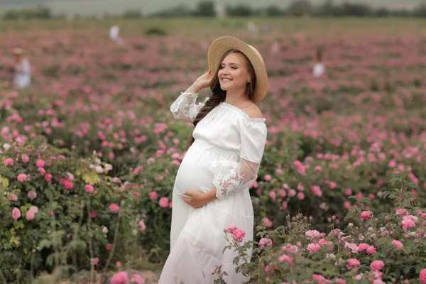 Pregnant woman in straw hat on her head stands in a flower field — Stock fotografie