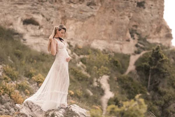 La sposa in una romantica passeggiata durante la gravidanza in estate passeggiate sugli scogli — Foto Stock