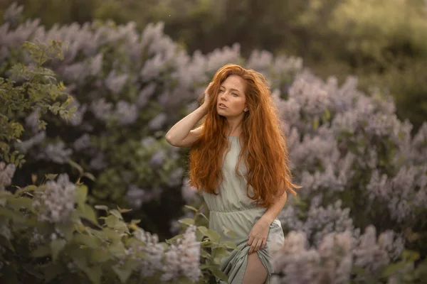 Çiçekler arasında uzun kızıl saçlı bir kadın. — Stok fotoğraf