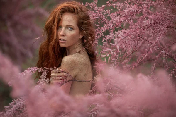 Çiçekler arasında uzun kızıl saçlı bir kadın. — Stok fotoğraf