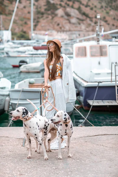 Chica camina con mascota, adulto dálmata en el paseo marítimo con el transporte acuático . —  Fotos de Stock