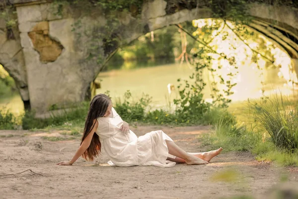 Gravid kvinna i lång vit klänning går barfota i skogen nära floden — Stockfoto