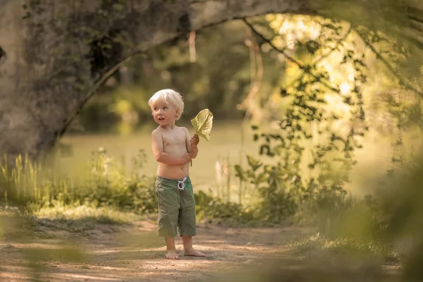 一个光着脚穿着短裤的4岁男孩沿着河边的一条森林小路奔跑 — 图库照片