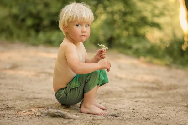 Seorang anak laki-laki berusia 4 tahun bertelanjang kaki dengan celana pendek berjalan di sepanjang jalan hutan dekat sungai — Stok Foto
