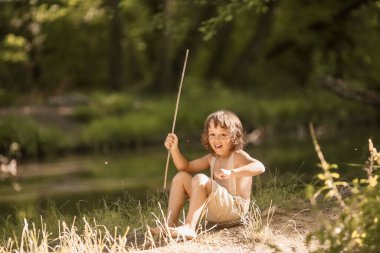 Nehrin kenarında elinde bir sopayla elinde olta olan bir çocuk..