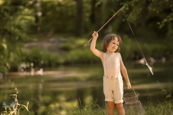 Un garçon près de la rivière avec un bâton dans les mains comme avec une canne à pêche . — Photo