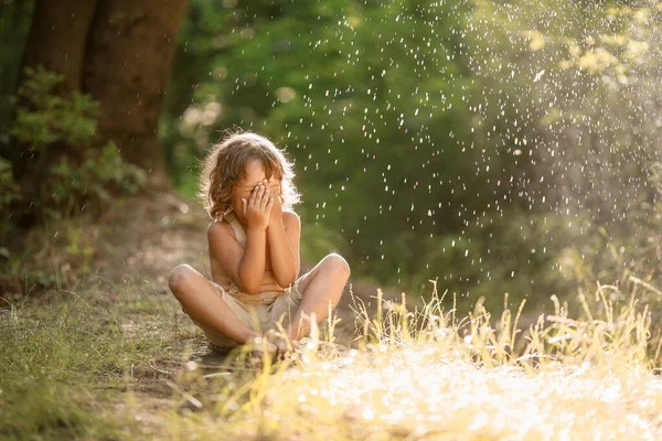 Un bambino siede a piedi nudi a terra lavato da gocce di rugiada — Foto Stock