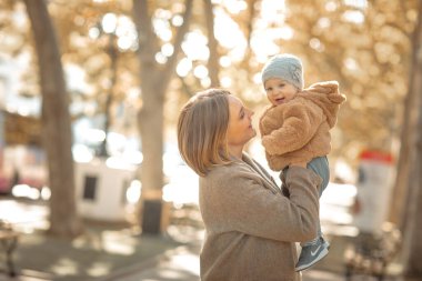 Anne ve çocuk halka açık bir parkta yürüyorlar kucaklaşıp öpüşüyorlar..