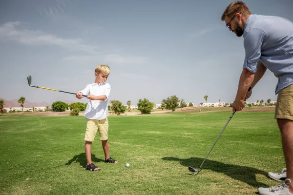 Padre se divierte y enseña a su hijo a jugar al golf en la hierba verde — Foto de Stock