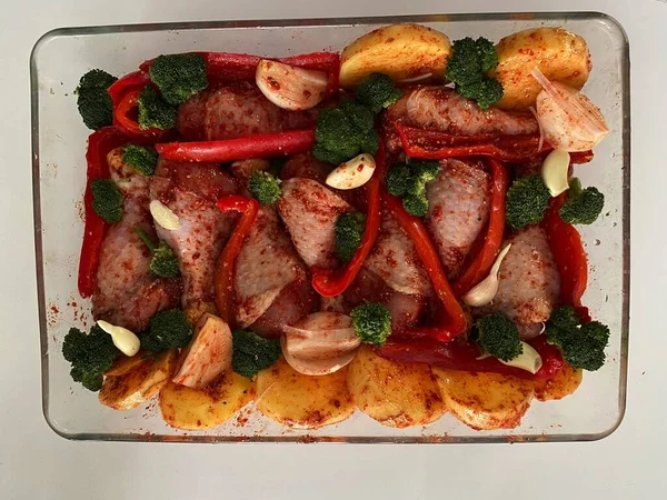 Saftige Hühnerschenkel mit Gemüse Brokkoli Kartoffeln und Knoblauch in einem Teller zum Backen bedeckt — Stockfoto