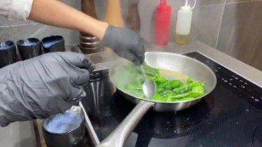 Aşçı metal bir tavada ıspanak yapraklarını kızartır ve karıştırır.