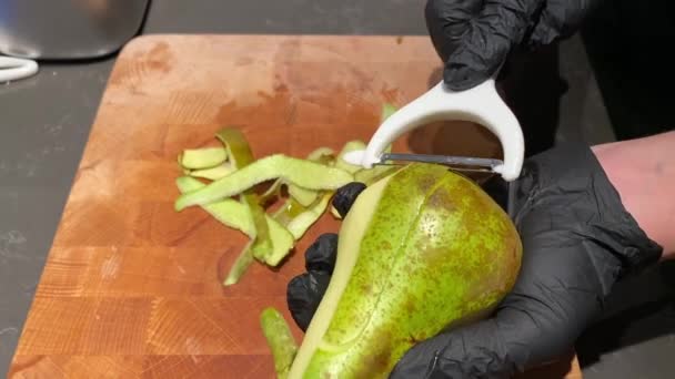 Жінка в чорних кухонних рукавичках очищає шкірку груші ріжучим ножем — стокове відео