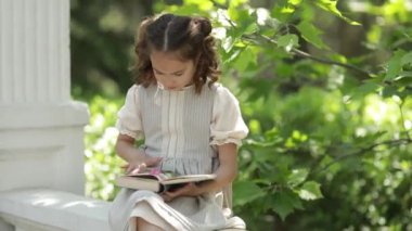 Okul üniformalı bir kız beton merdivenlerde oturup kitap okuyor.
