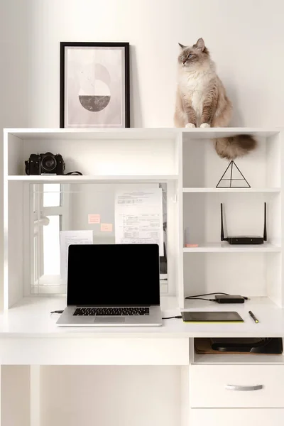 Beyaz ofis içi, dizüstü bilgisayarı ve rafında çelenk olan rahat bir iş yeri.