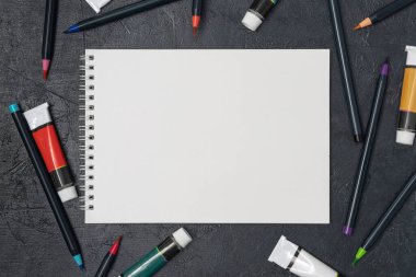 Eskiz defteri, resim ve suluboya fırçaları olan bir ressam masası.