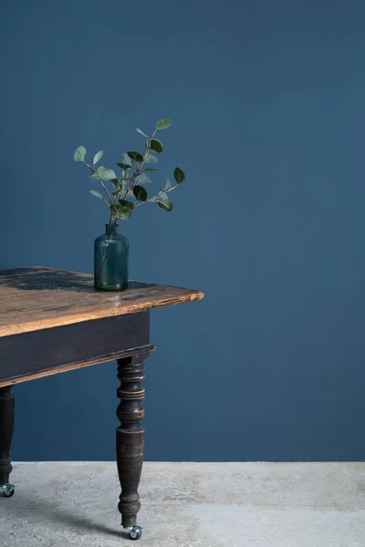 Minimalist tavan arası, ahşap bir masadaki vazoya yerleştirilmiş koyu mavi bir duvara karşı.