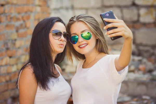 Namoradas tirando uma selfie no contexto urbano da cidade. Conceito de amizade e diversão com novas tendências e tecnologia — Fotografia de Stock