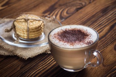 A cup of coffee and small cookies on an antique wooden table clipart