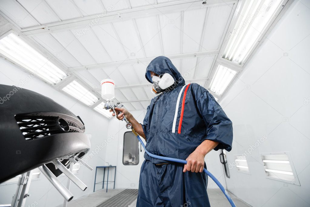 Worker painting a car black blank parts in special garage, wearing