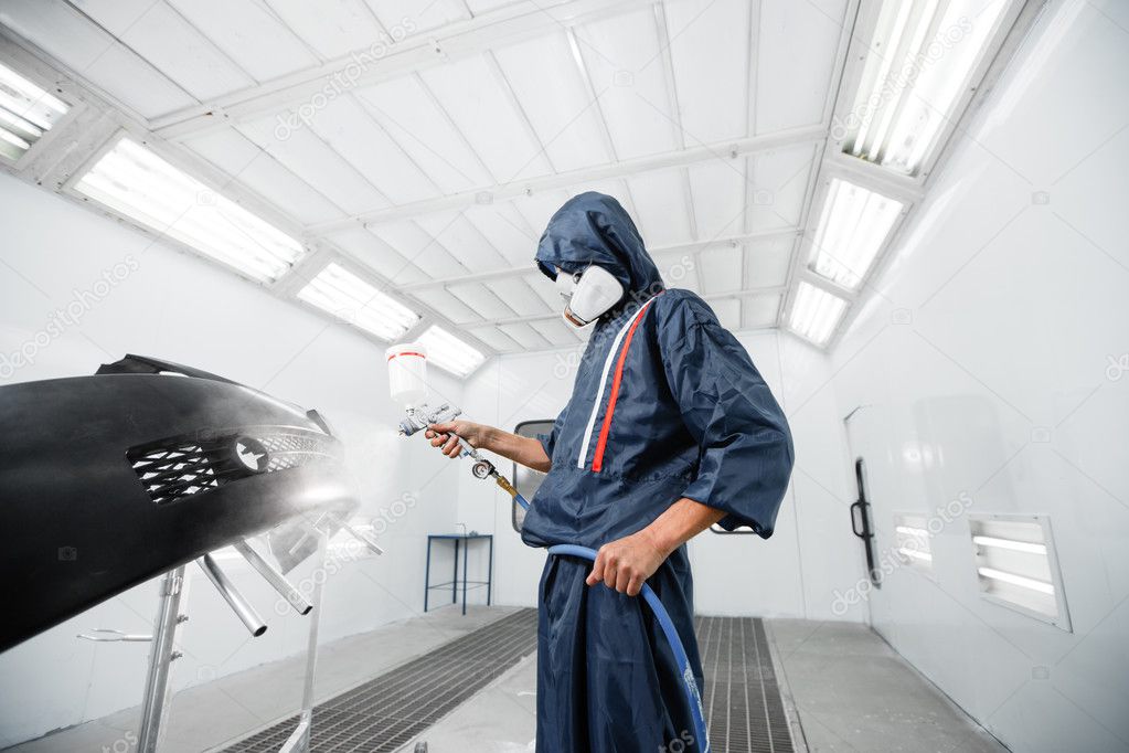 worker painting a car black blank parts in special garage, wearing costume and protective gear
