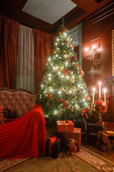 Noche de Navidad a la luz de las velas. apartamentos clásicos con chimenea blanca, árbol decorado, sofá, grandes ventanales y lámpara de araña . —  Fotos de Stock