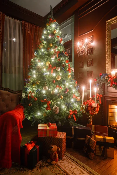 圣诞烛光晚会。与白色的壁炉、 装饰的树、 沙发、 大窗户和枝形吊灯经典公寓. — 图库照片