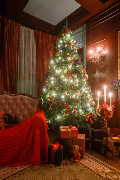 Vánoční večer při svíčkách. Klasické apartmány s bílým krbem, nazdobený stromeček, pohovka, velkými okny a lustr. Royalty Free Stock Fotografie